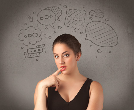 A cute female student making funny expressions with thoughts in her head illustrated by drawn chat bubbles on the urban wall background concept.の写真素材