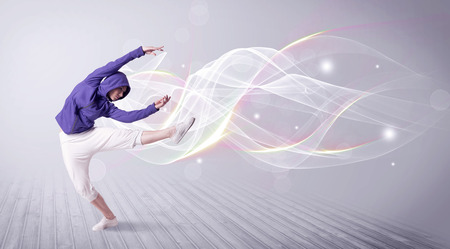 A beautiful young hip hop dancer dancing contemporary urban street dance in front of grey wall background with smokey lines and glitter concept.の写真素材