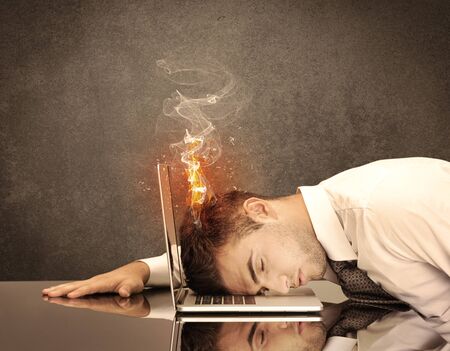 A frustrated businessman resting his head on a keyboard and shouting with his hair on smoke, catching fireの写真素材
