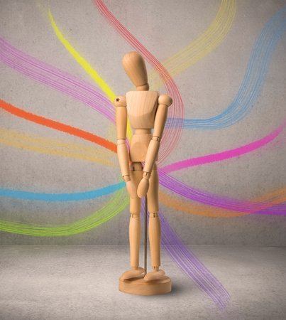Wooden mannequin posed in front of a greyish background with colorful lines behind itの写真素材