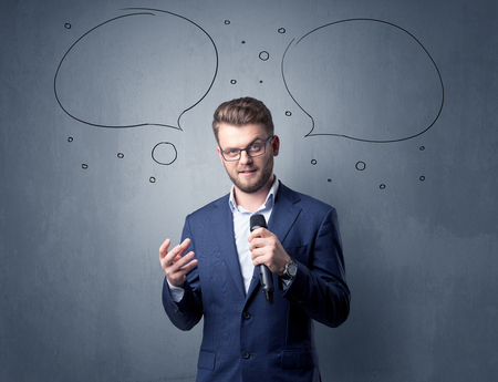 Businessman speaking into microphone with speech bubbles over his headの写真素材