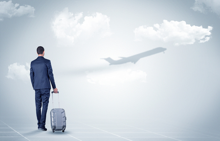 Young businessman with luggage walking towards an looking to a raising airplane
の写真素材