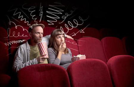 Young cute couple sitting in cinema, and eating popcorn while watching movie with doodle graphicsの写真素材