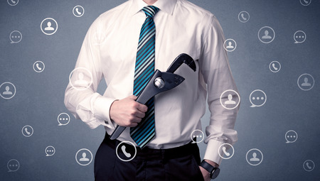 Thoughtful businesman holding tool with communication symbols aroundの写真素材