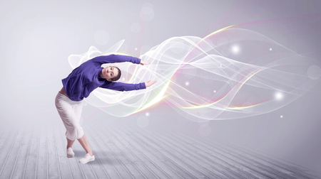 A beautiful young hip hop dancer dancing contemporary urban street dance in front of grey wall background with smokey lines and glitter concept.の写真素材