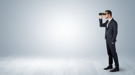 Businessman looking forward with binoculars in an empty spaceの写真素材