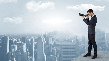 Businessman looking forward to a city  with binoculars from skyscraper concept
の写真素材