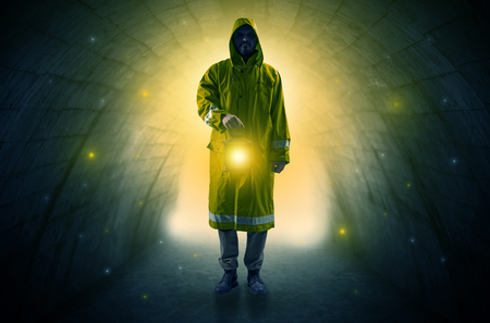 Ugly man in raincoat walking with glowing lantern in a dark tunnelの写真素材