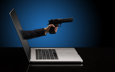 Hand with gun coming out of a laptopの写真素材