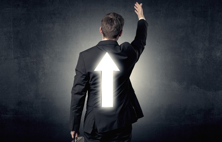 Young businessman standing with arrow on his backの写真素材
