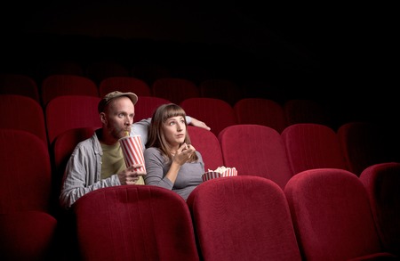Young couple sitting at red movie theatreの写真素材