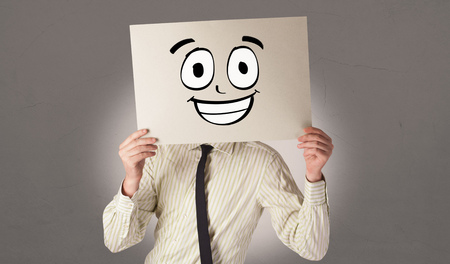 Student holding a paper with laughing emoticon in front of his faceの写真素材