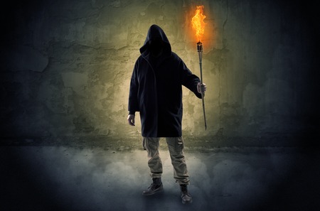 Ugly wayfarer with burning torch in his hand in front of a crumbly wall conceptの素材 FY310119157628