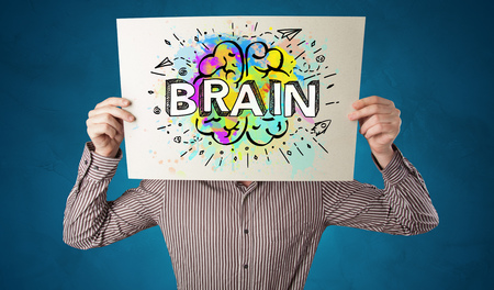 Young person holding white paper in front of her head with colorful brain conceptの写真素材