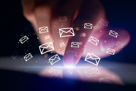 Finger touching tablet with white drawn mail icons above and dark backgroundの写真素材