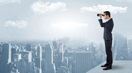 Businessman looking forward to a city with binoculars from skyscraper conceptの販売画像