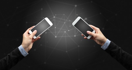 Close up of two hands holding smartphones to each other, wireless connection conceptの写真素材