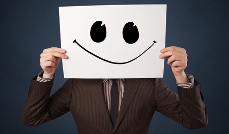 Casual person holding a paper with funny emoticon in front of her faceの写真素材