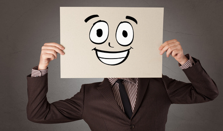 Young student holding a paper with laughing emoticon in front of his faceの写真素材