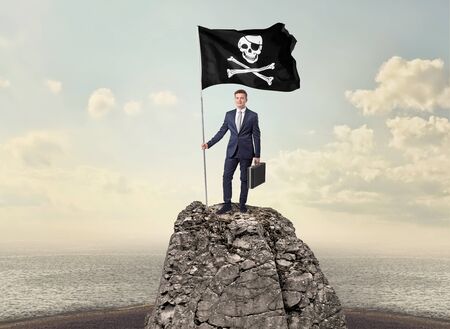 Successful businessman on the top of a mountain holding pirate flagの写真素材