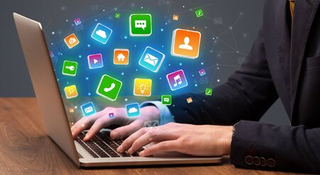 Businessman hand typing on laptop with flying application icons aroundの写真素材