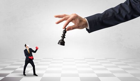 Small businessman fighting against big chessman on a big hand with chess board conceptの写真素材