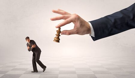 Small frail businessman with suitcase running away from big hand with chessman conceptの写真素材