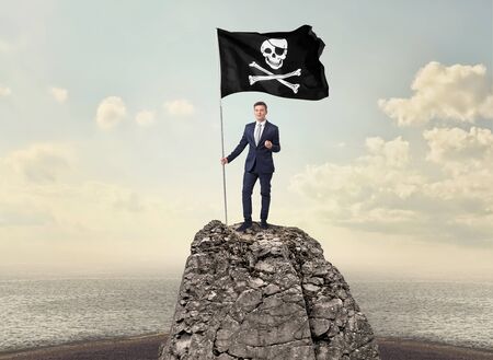 Successful businessman on the top of a mountain holding pirate flagの写真素材
