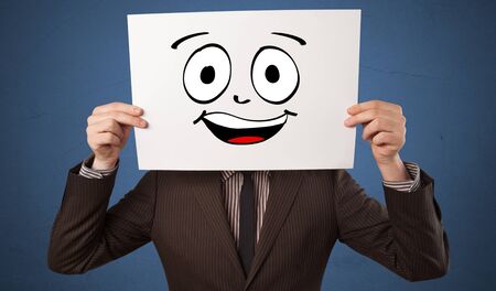 Young student holding a paper with laughing emoticon in front of his faceの写真素材