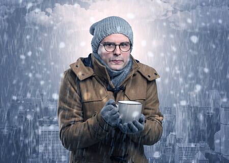 Young man freezing in warm clothing with city conceptの写真素材