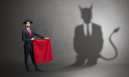 Businessman standing with red cloth in his hand and devil shadow on the backgroundの写真素材