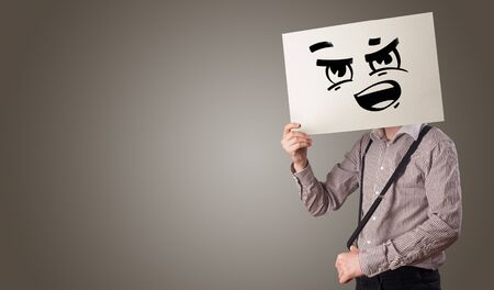 Casual person holding a paper in front of his face with drawn emoticon faceの写真素材