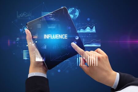 Businessman holding a foldable smartphone with INFLUENCE inscription, successful business conceptの写真素材