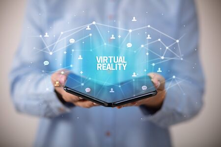Businessman holding a foldable smartphone with VIRTUAL REALITY inscription, new technology conceptの写真素材