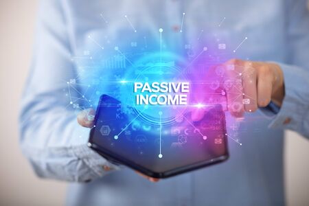 Businessman holding a foldable smartphone with PASSIVE INCOME inscription, new business conceptの写真素材