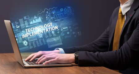 Businessman working on laptop with TECHNOLOGY IMPLEMENTATION inscription, cyber technology conceptの写真素材
