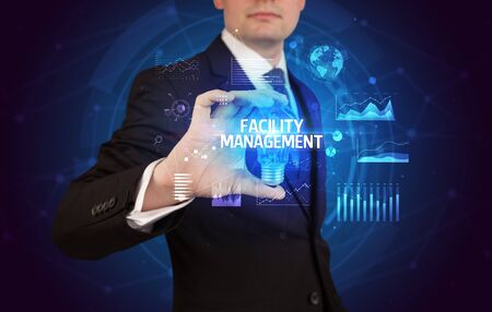 Businessman holding lightbulb with FACILITY MANAGEMENT inscription, Business idea conceptの写真素材