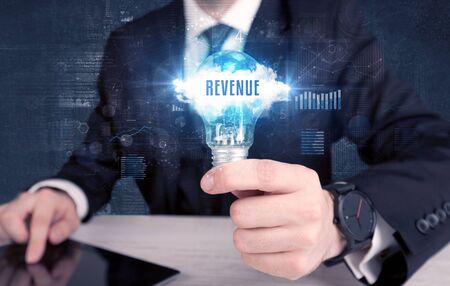 Businessman holding a light bulb with REVENUE inscription, new business conceptの写真素材