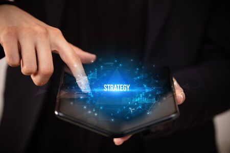 Businessman holding a foldable smartphone with STRATEGY  inscription, business concept
の写真素材