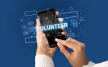 Female hand typing on smartphone with VOLUNTEER inscription, social media conceptの写真素材