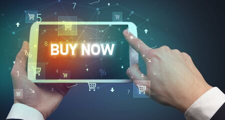 Close-up of a hand holding tablet with BUY NOW inscription, online shopping conceptの写真素材