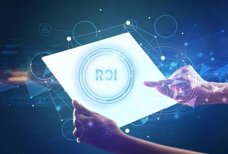 Hand holdig futuristic tablet with ROI  inscription, modern technology conceptの写真素材