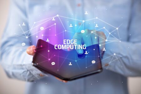 Businessman holding a foldable smartphone with EDGE COMPUTING inscription, new technology conceptの写真素材