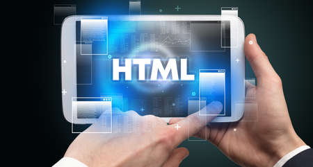 Close-up of a hand holding tablet with HTML abbreviation, modern technology conceptの写真素材