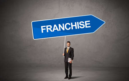 Young business person in casual holding road sign with FRANCHISE inscription, new business direction conceptの写真素材