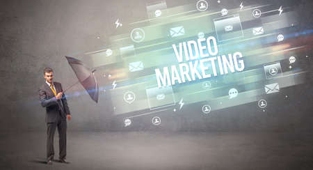 Handsome businessman defending with umbrella from VIDEO MARKETING inscription, new age media conceptの写真素材