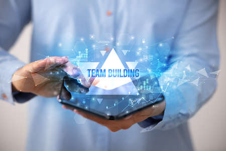 Businessman holding a foldable smartphone with TEAM BUILDING inscription, business concept