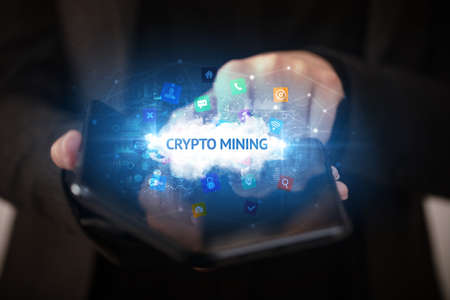 Businessman holding a foldable smartphone with CRYPTO MINING inscription, technology conceptの写真素材
