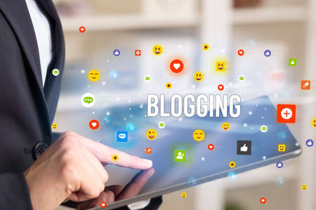 Close up of business person playing multimedia with social media icons and BLOGGING inscriptionの写真素材