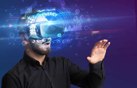 Businessman looking through Virtual Reality glasses with ENERGY inscription, innovative technology...